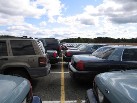 1991 Ford LTD Crown Victoria - A line of dark 1991 Ford Crown Victoria LTD sedans are parked in a lot under a cloudy sky.