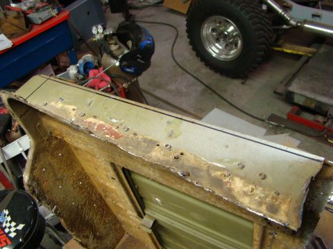 1948 Jeep Wrangler - A close-up view of a corroded metal panel undergoing repair, showing drill holes and cut edges.