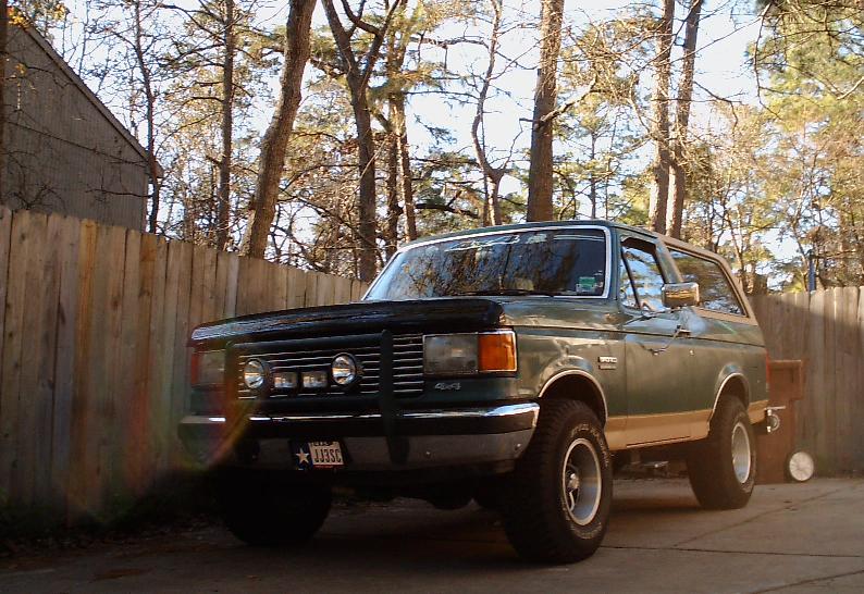 Green Ford Bronco 4x4 with chrome bumper parked by a wood fence in fall