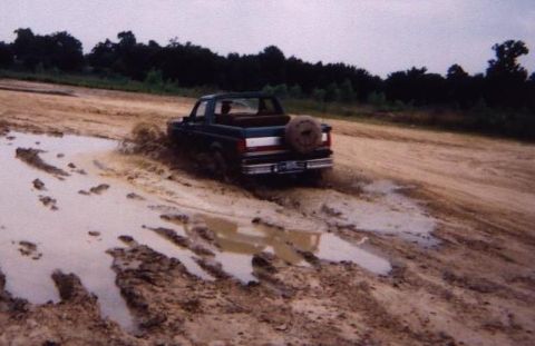 1989 Ford Bronco - A Ford Bronco navigates a muddy track, kicking up water and dirt.