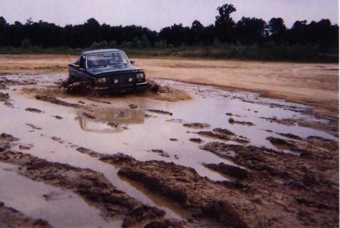Dark topless Ford Bronco driving head-on through a flooded mud pit in a sand pit