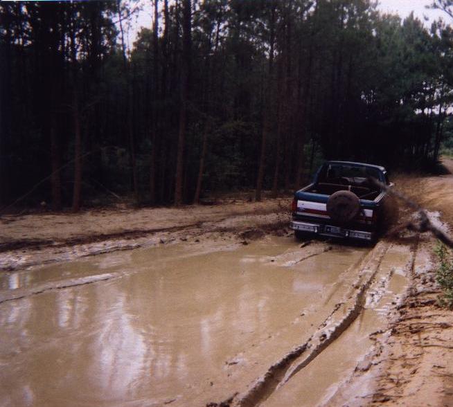 Dark pickup truck driving through a muddy forest trail mud pit