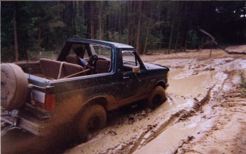 1989 Ford Bronco - Ford Bronco navigating a challenging muddy track with trees in the background.