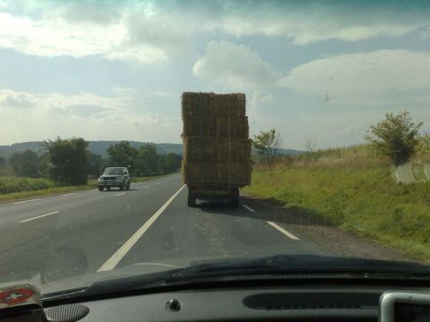 1991 Ford Crown Victoria - A silver SUV travels down a highway, passing a large truck loaded with hay bales under a cloudy sky.