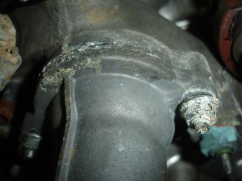 1993 Ford Taurus - This image shows a heavily corroded engine part, likely a thermostat housing or intake manifold, with significant buildup around a bolt hea…