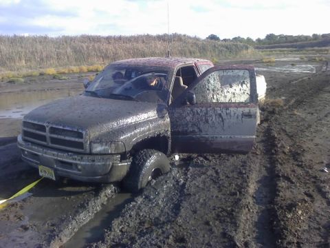 1996 Dodge 1500 - This Dodge 1500 is deeply stuck in thick mud, with its doors open, suggesting a difficult off-road situation.