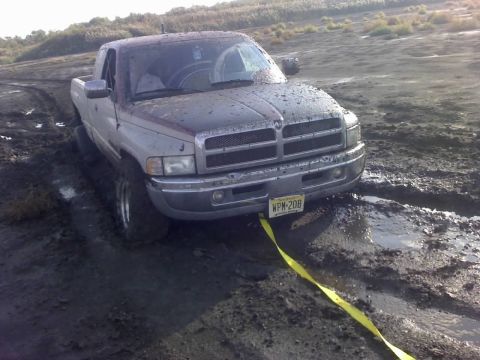 1996 Dodge 1500 - A mud-splattered Dodge Ram pickup truck is stuck in a muddy terrain, with a tow strap attached to its front.