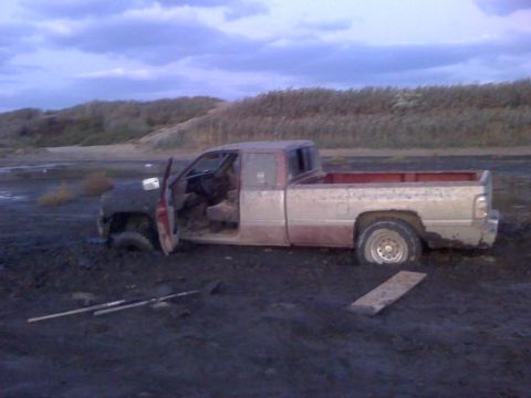 1996 Dodge 1500 - A weathered pickup truck is deeply mired in dark, wet earth, with its driver's side door ajar.