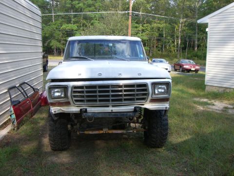 1988 Ford Bronco - A white Ford truck is parked in front of a building, showing its front grille and lifted suspension.