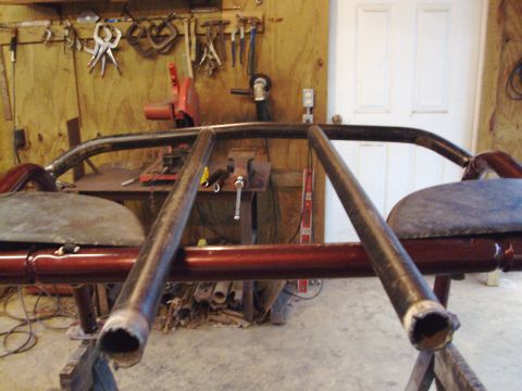 1995 Ford Bronco - Custom roll cage structure with red painted tubing and gray upholstered seats, seen in a workshop.