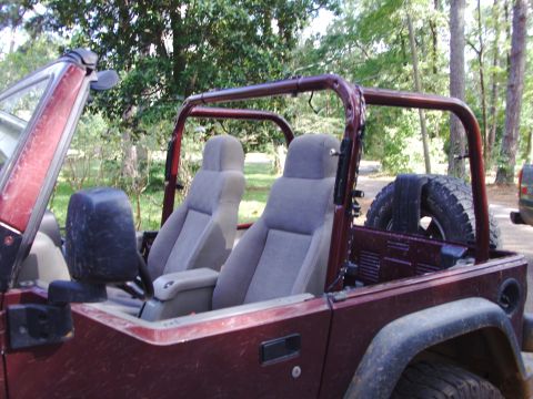 1995 Ford Bronco - The interior of a maroon Jeep shows grey seats and a roll cage, with a spare tire visible at the back.