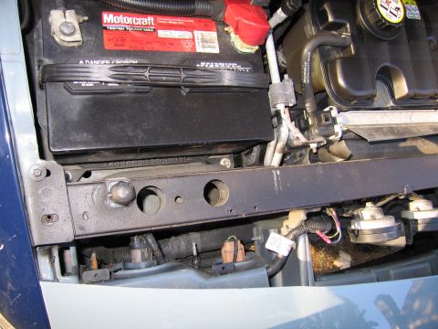 1991 Ford LTD Crown Victoria - Close-up view of a car battery and engine bay components, showing hoses and wiring.