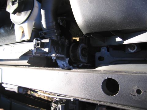 1991 Ford LTD Crown Victoria - Close-up view of a damaged bracket on the radiator support, with a hose visible.