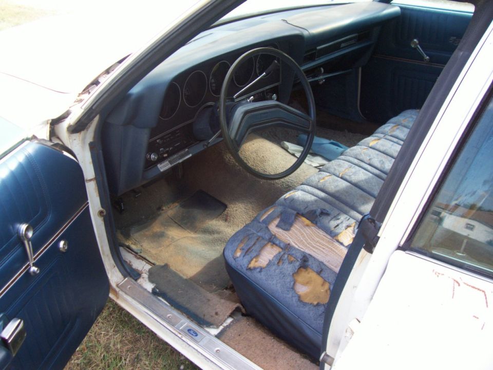 Worn blue interior of an old car with bench seat, steering wheel and exposed floor