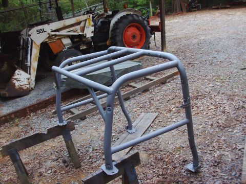 1995 Ford Bronco - A gray roll cage is shown mounted on sawhorses, with a tractor and loader visible in the background.
