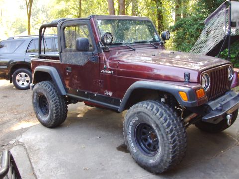 1995 Ford Bronco - Maroon Jeep Wrangler with roll cage and off-road tires is parked outside.