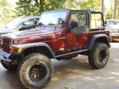 1995 Ford Bronco - A red Jeep Wrangler is parked outdoors, with another vehicle partially visible behind it.