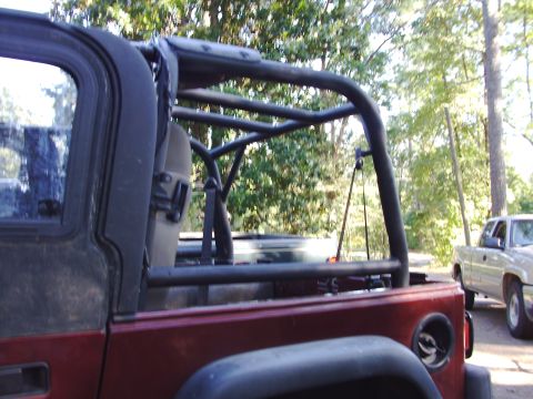 1995 Ford Bronco - Side view of a red SUV with an aftermarket roll cage, with another truck visible in the background.
