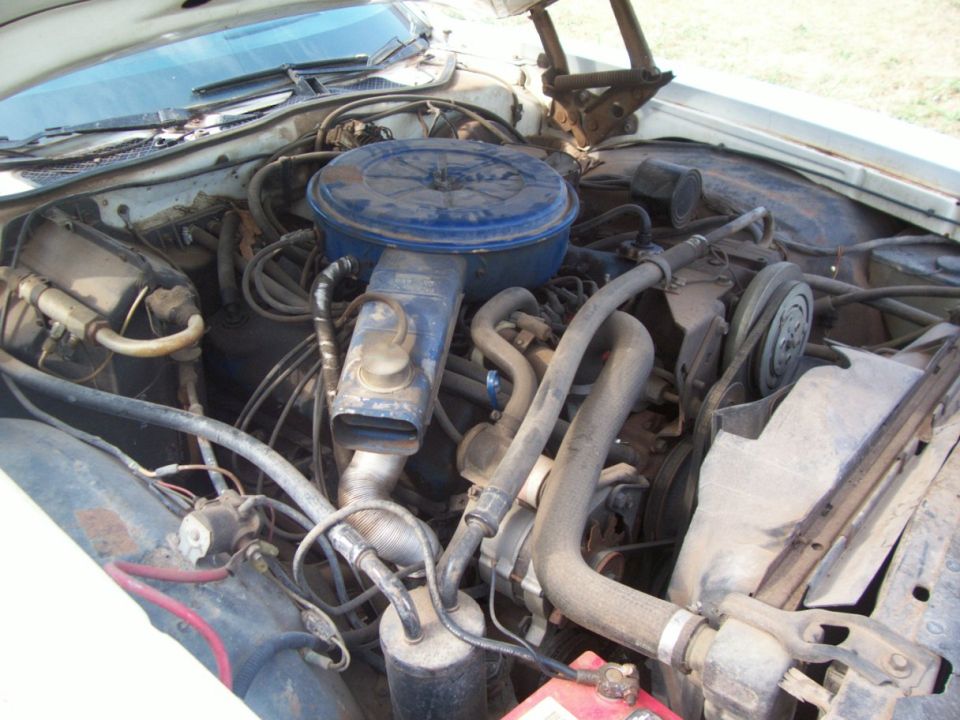 Dusty older V8 engine bay with blue air cleaner under raised hood
