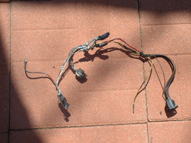 Old wiring harness with taped splices and connectors laid on red brick pavers
