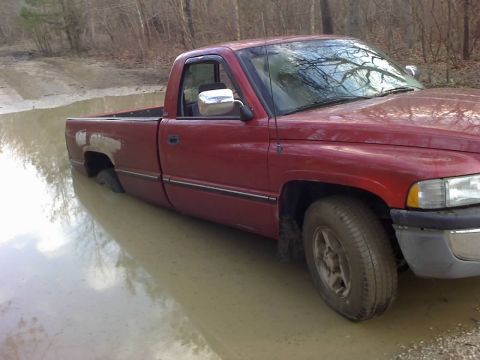 1996 Dodge 1500 - A red pickup truck is stuck in a muddy puddle, with its rear wheel submerged.