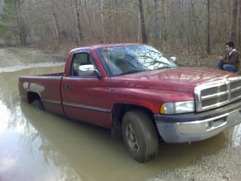 1996 Dodge 1500 - A red 1996 Dodge 1500 pickup truck is partially submerged in muddy water in a wooded area.