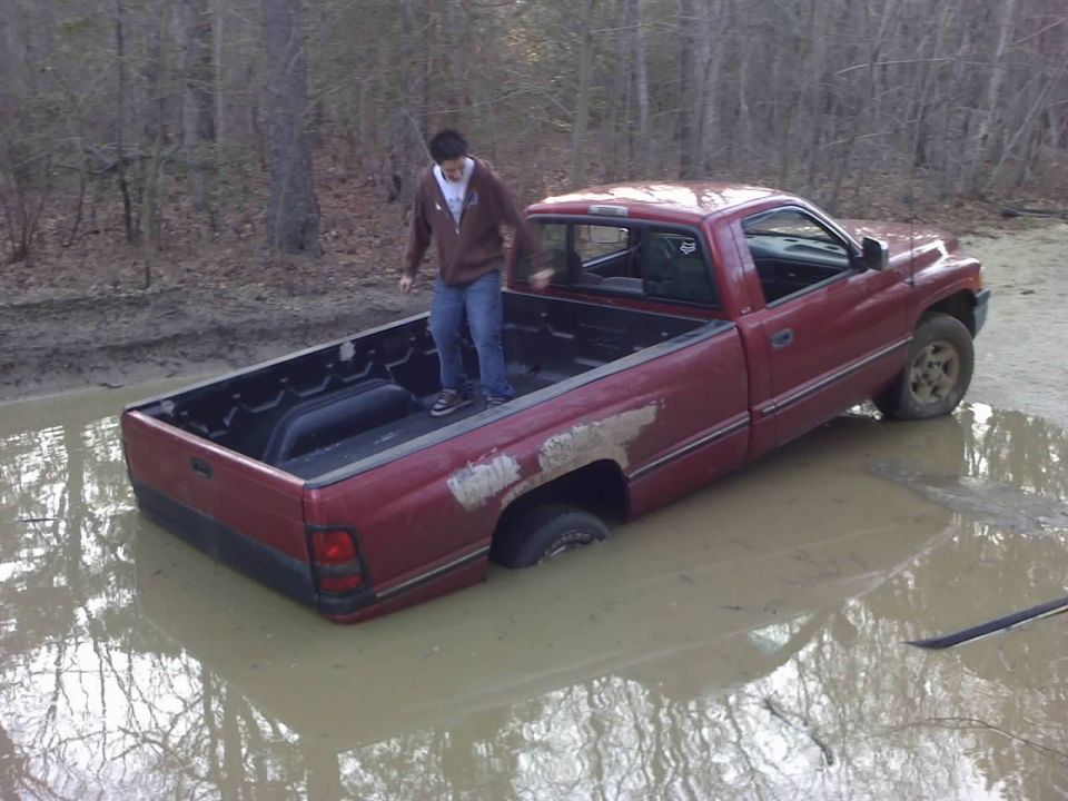 Red pickup truck stuck in a mud puddle with a guy standing in the bed. Looks like a 1994 Dodge Ram