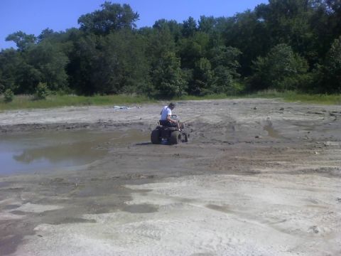 1996 Dodge 1500 - A person rides an ATV through a muddy, off-road area under a clear blue sky.