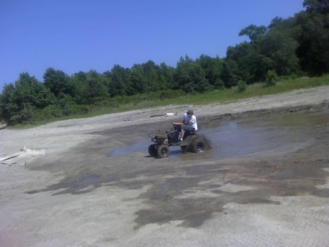 1996 Dodge 1500 - A person rides a modified lawn tractor through a muddy area on a sunny day.