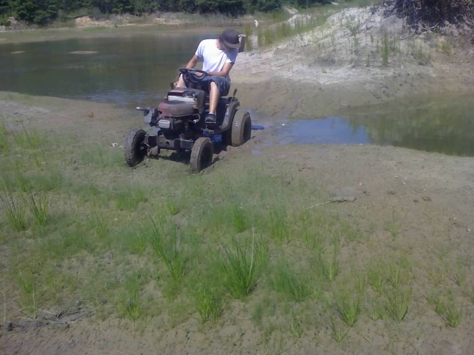 Man on riding mower stuck in muddy bank near water