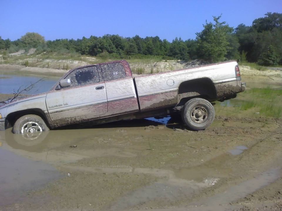 Silver pickup truck stuck in mud, side view. Appears to be a 1994 Dodge Ram 1500