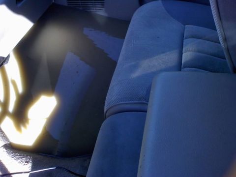 1996 Dodge 1500 - The interior of a vehicle shows blue fabric seats and a dark floor with water damage, with a center console in view.