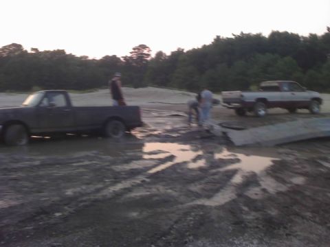 1996 Dodge 1500 - Two pickup trucks are stuck in a muddy area with trees in the background.
