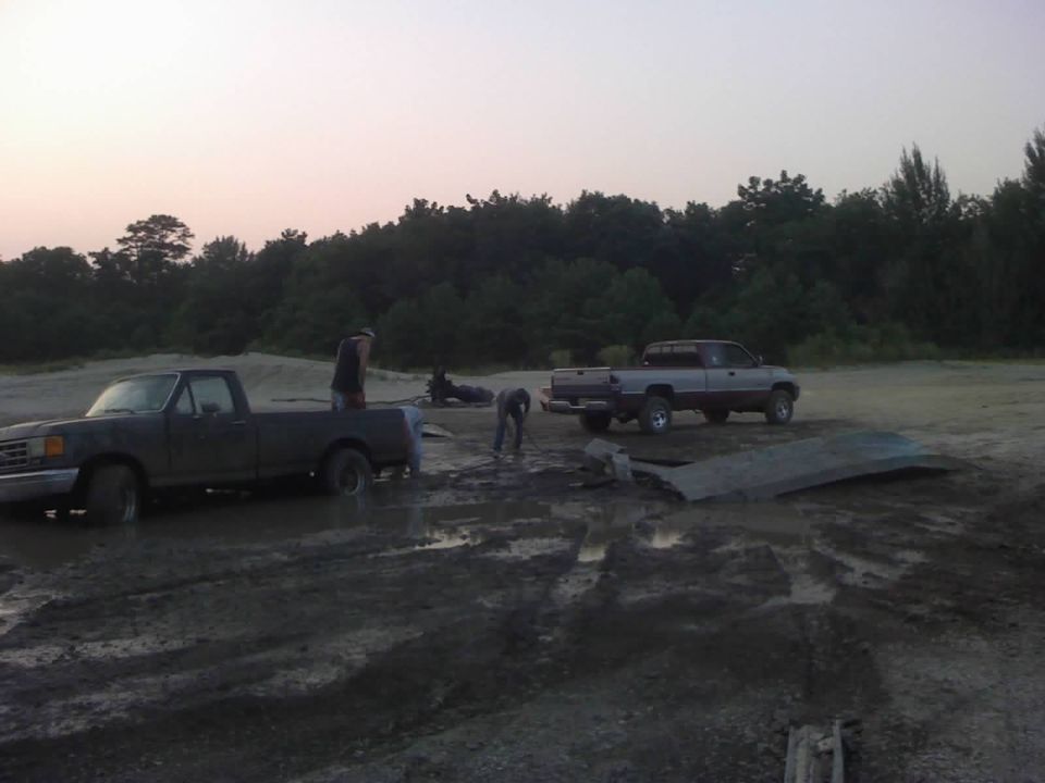 two pickup trucks stuck in mud with people around