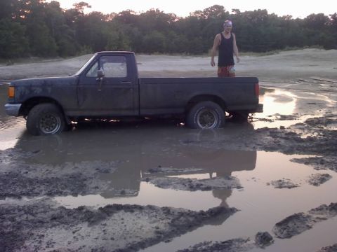 1996 Dodge 1500 - A dark pickup truck is stuck in a muddy area with a man standing in the bed.
