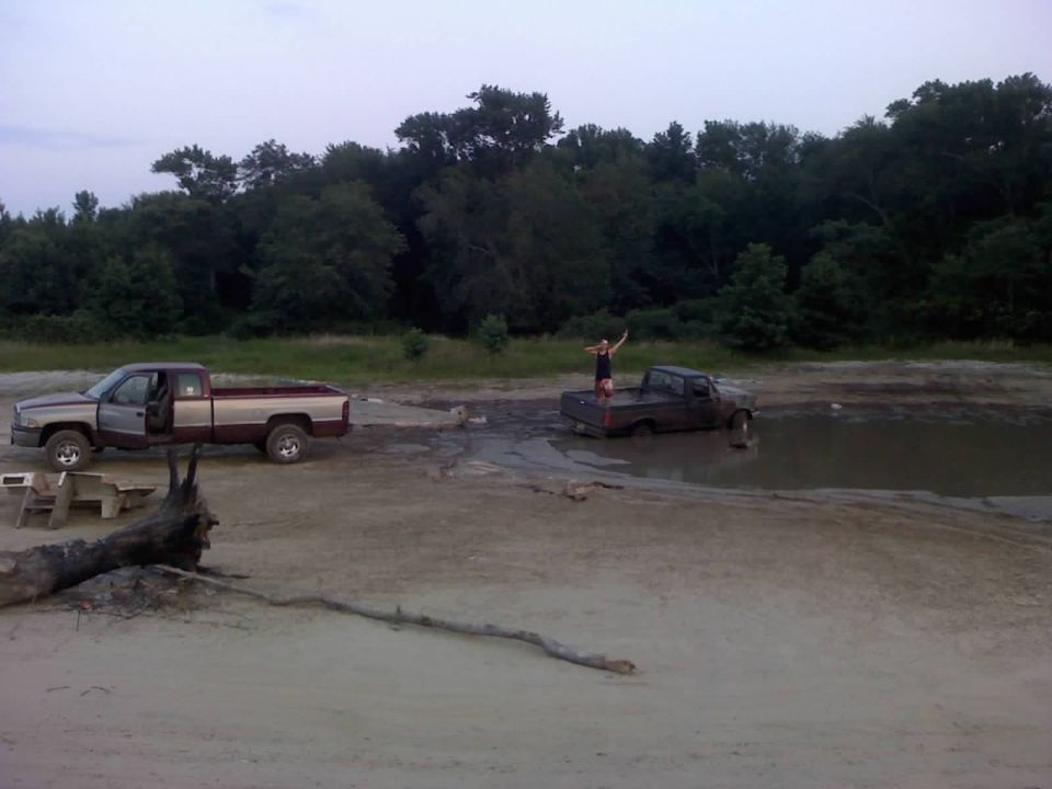 Two pickup trucks in a muddy area with people standing on them