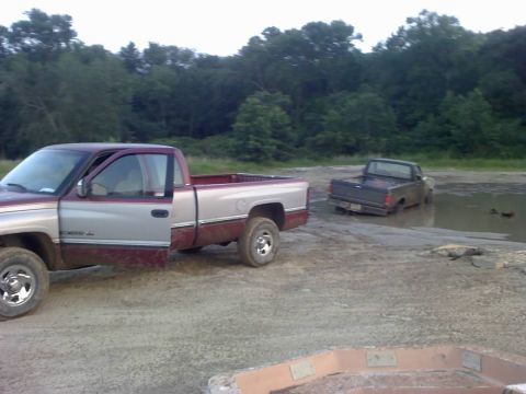 1996 Dodge 1500 - Two pickup trucks are in a muddy outdoor area, with one truck partially submerged.