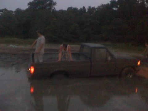1996 Dodge 1500 - A dark pickup truck is stuck in a muddy area with two people nearby.