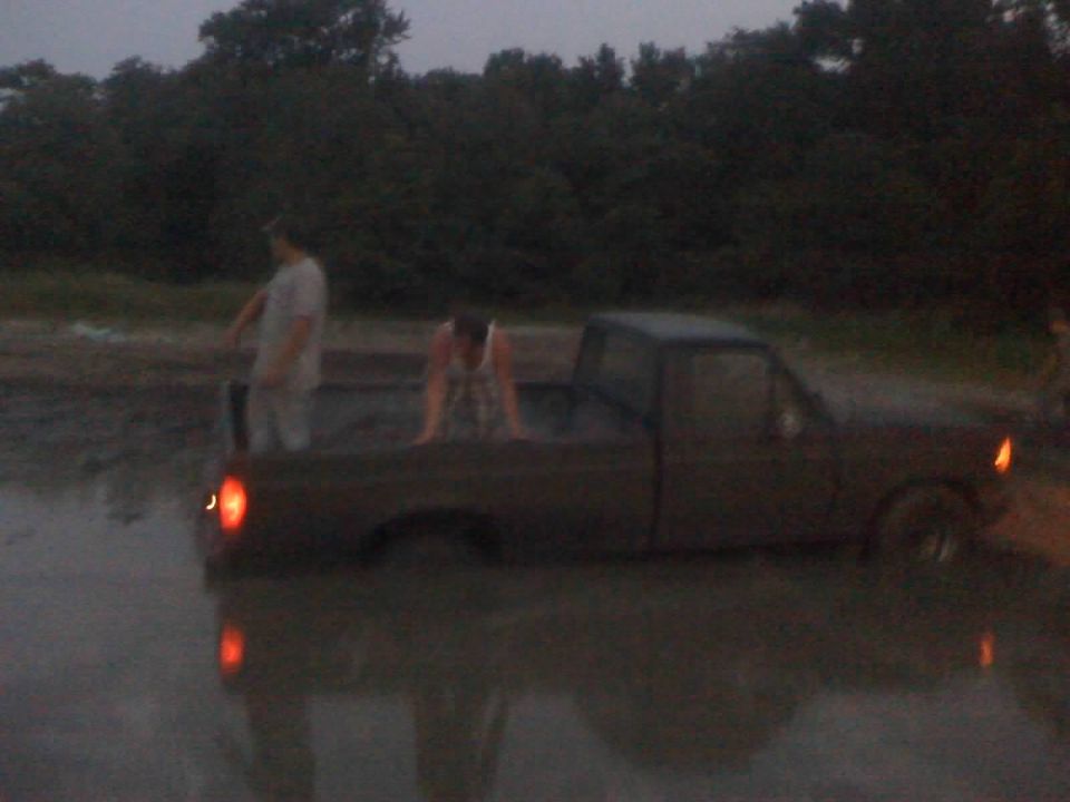 Dark pickup truck stuck in muddy water, with two people near it