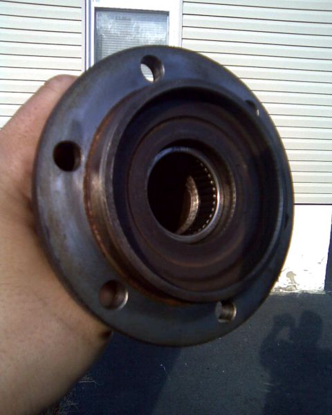 1989 Ford Bronco - A close-up view of a wheel hub assembly, held by a hand, with a building in the background.