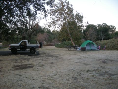 1991 Ford Bronco - A two-tone SUV with its top removed is parked at a campsite next to a tent and picnic table.