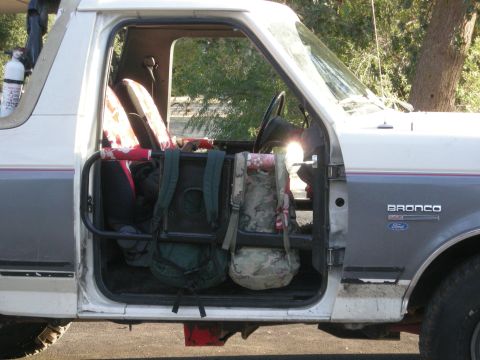 1991 Ford Bronco - The side of a 1991 Ford Bronco shows its interior with backpacks and a roll cage visible through the open door.