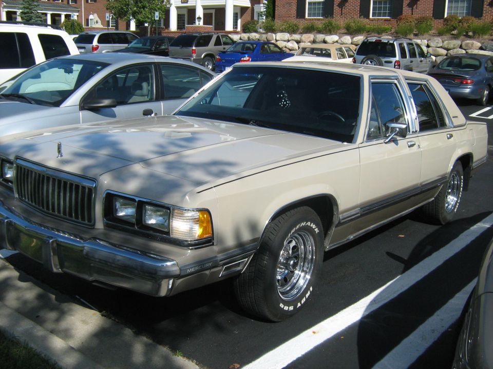 Tan 1988 Mercury Grand Marquis sedan parked in a lot, front 3/4 view, chrome wheels, slight damage on front bumper