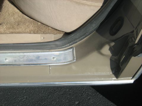 1988 Mercury Grand Marquis - Close-up of a car's interior door sill and carpet, showing the door seal and chrome trim.