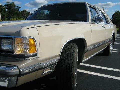 1988 Mercury Grand Marquis - The front fender and headlight assembly of a tan Mercury Grand Marquis are visible in this close-up shot.