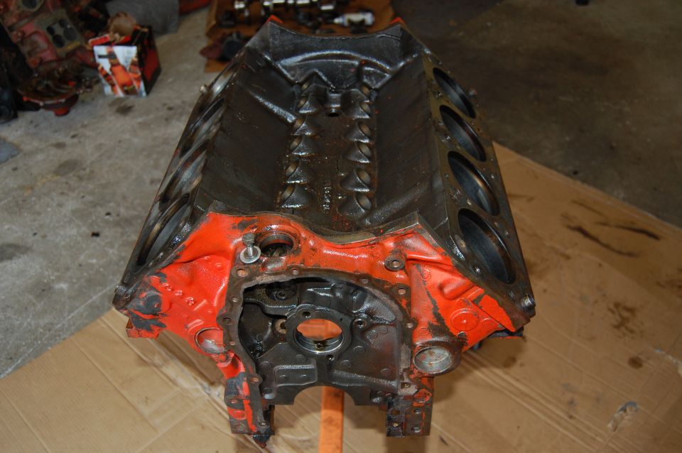 Orange and black engine block on a wooden surface. Other engine parts are visible in the background