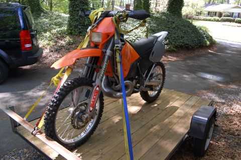 1994 Ford Bronco - An orange dirt bike is strapped to a trailer, with a black SUV nearby.