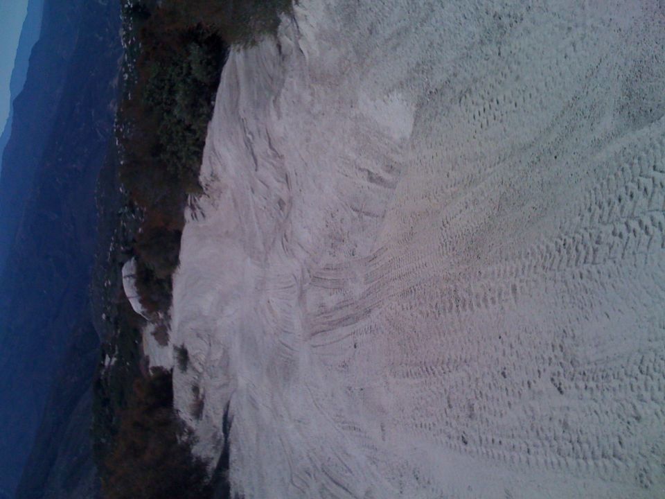 Tire tracks in sand with vegetation on the left and a watermark for SUPERMOTORS.NET