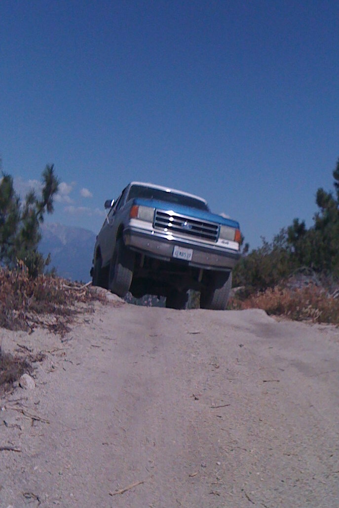 Blue and white Ford F-Series truck driving up a dirt hill