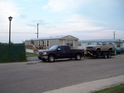 1996 Ford Bronco - A tan 1992 Ford Bronco is transported on a trailer towed by a dark pickup truck, with mobile homes in the background.
